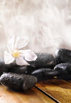 Group of black stones on wood base, steam background. Sauna, therapy, relaxation, and health concept.Vertical composition.